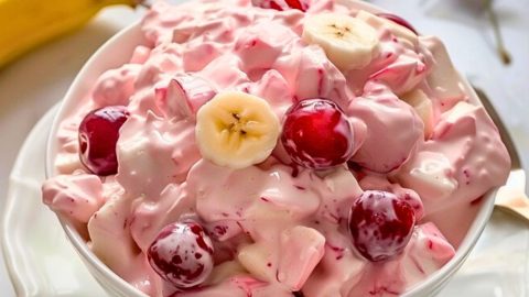 Creamy salad with cherry pie filling and fruit cocktail in a white bowl.