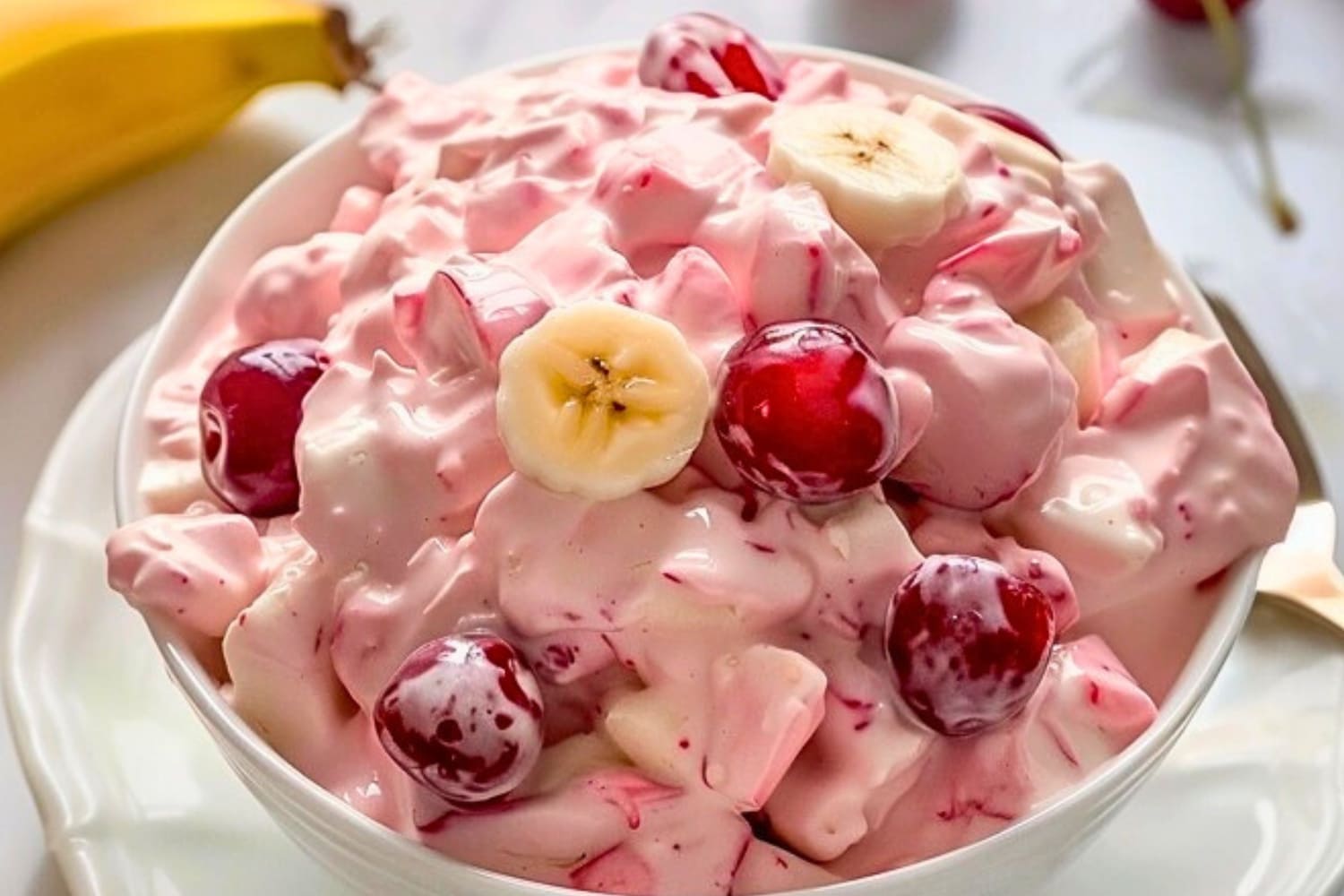 Creamy salad with cherry pie filling and fruit cocktail in a white bowl.