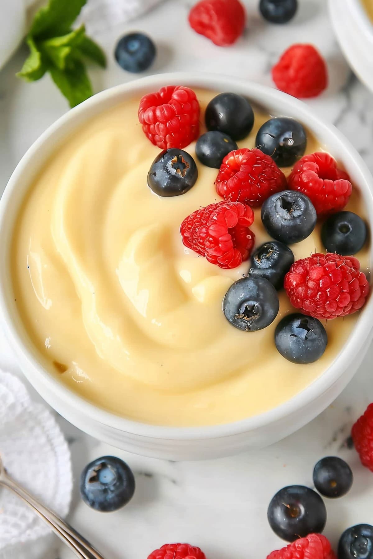 A delectable serving of vanilla custard, beautifully presented with fresh blueberries and raspberries in a white bowl