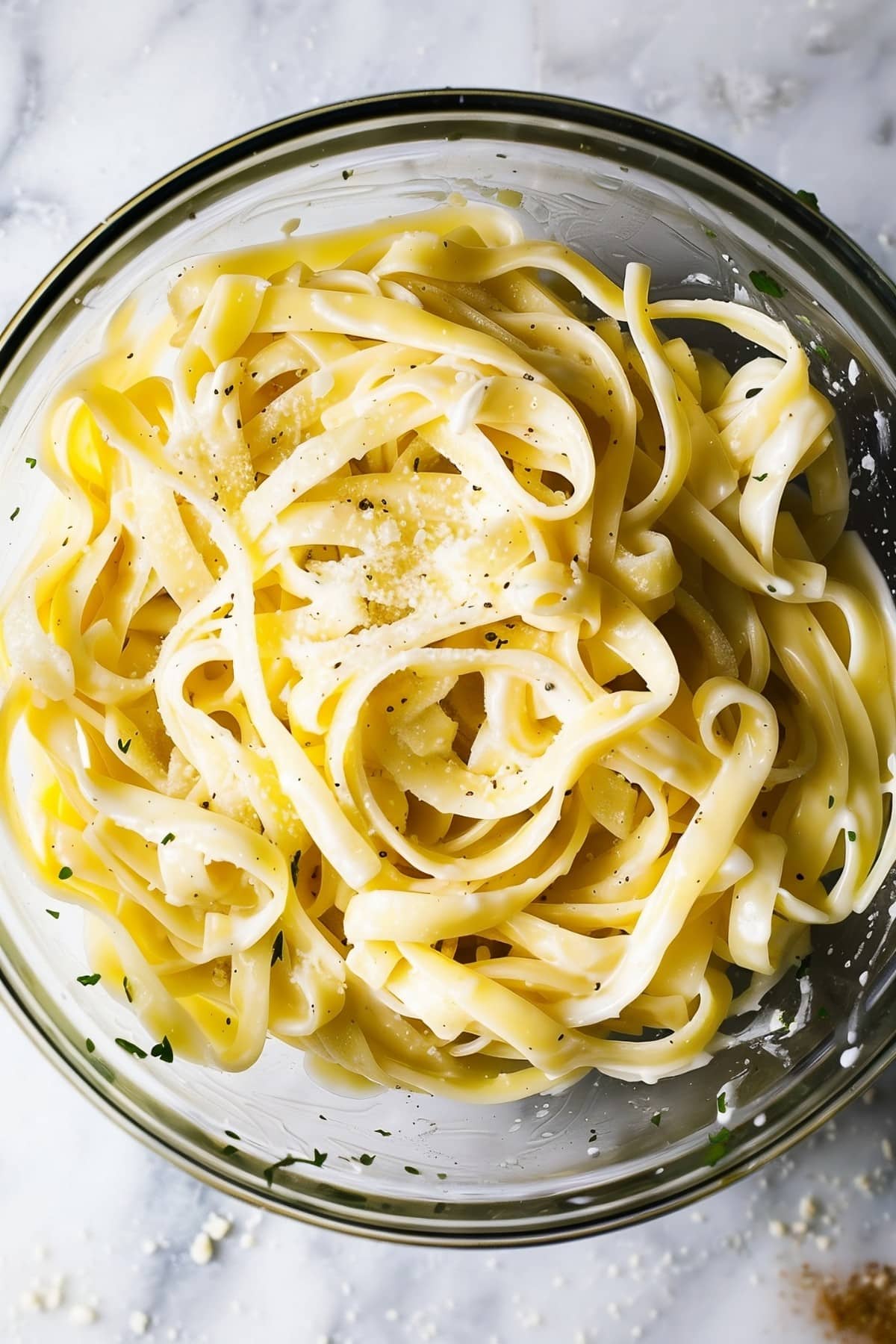 Creamy fettucine alfredo in a large glass bowl on a white marble table