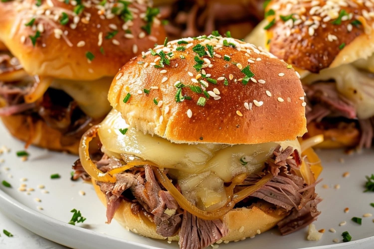 French dip sliders in a white plate with melted cheese sprinkled with sesame seeds.