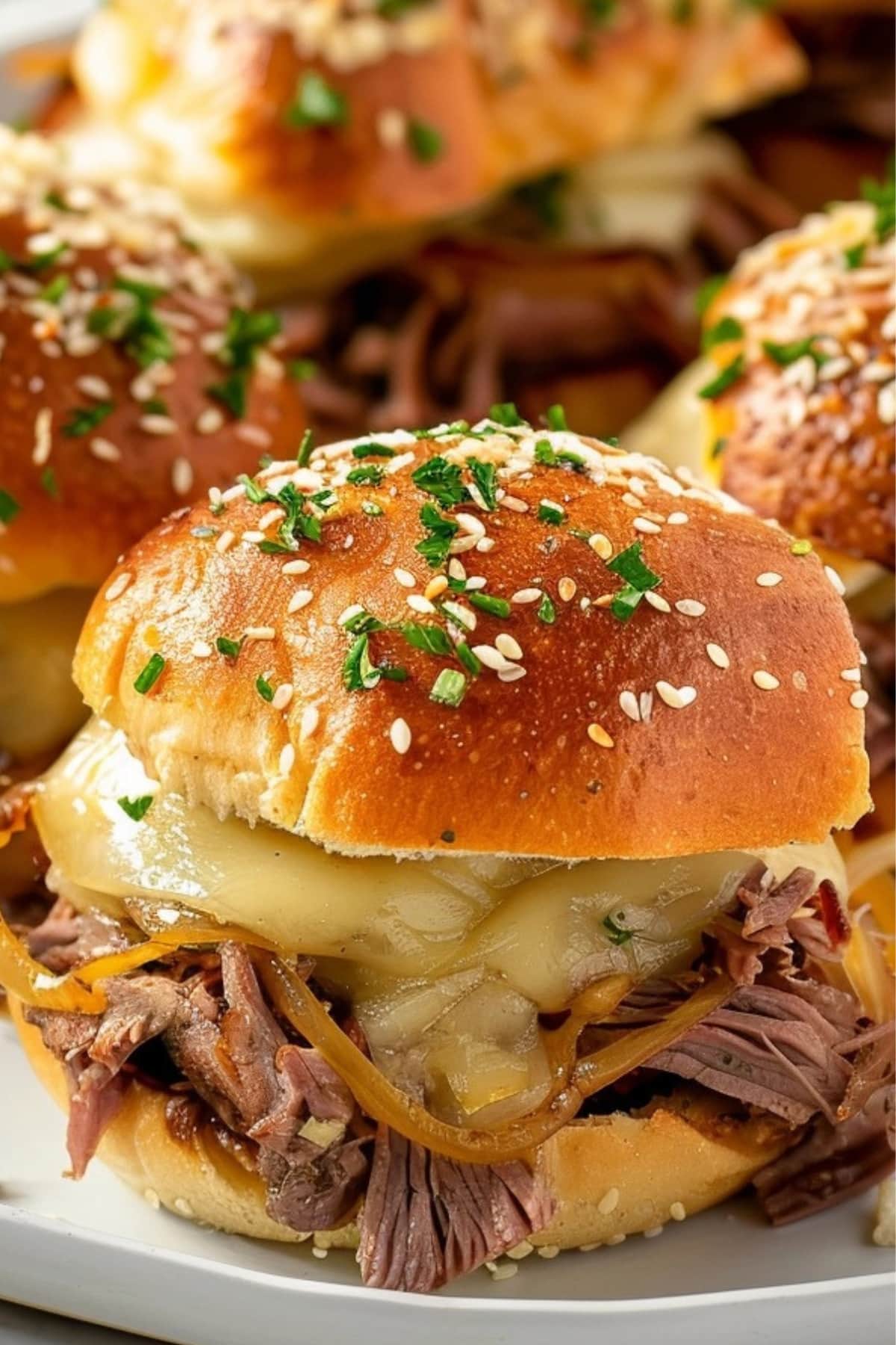 French dip sliders with roast beef, caramelized onion and cheese filling in a wooden board.
