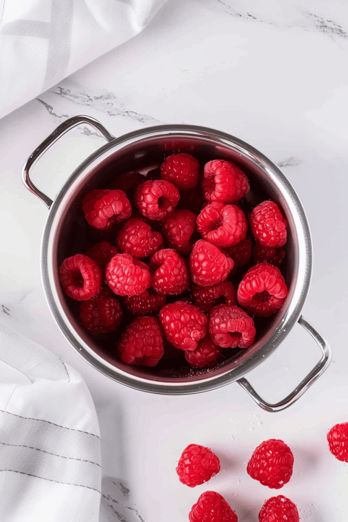 A container of fresh raspberries on a white marble table, overhead view