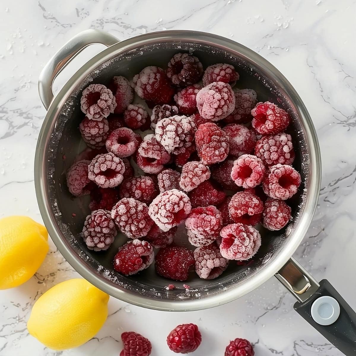 Frozen raspberries in a saucepan, lemon on the side.