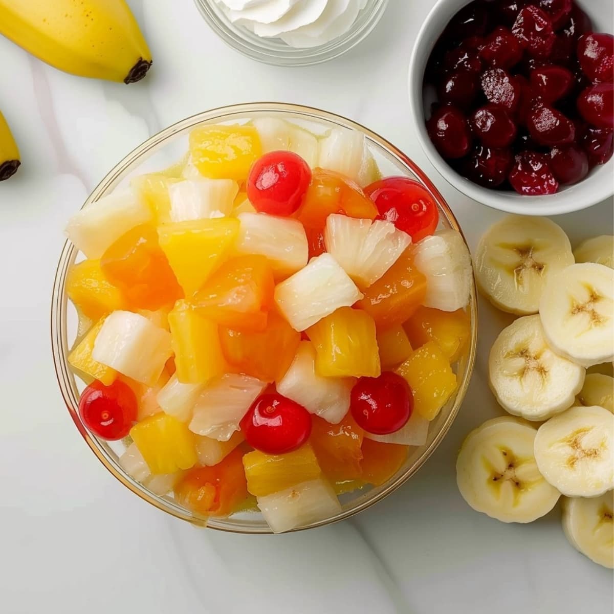 Fruit cocktail, cherry pie filling, banana and whipped cream on a white marble surface.