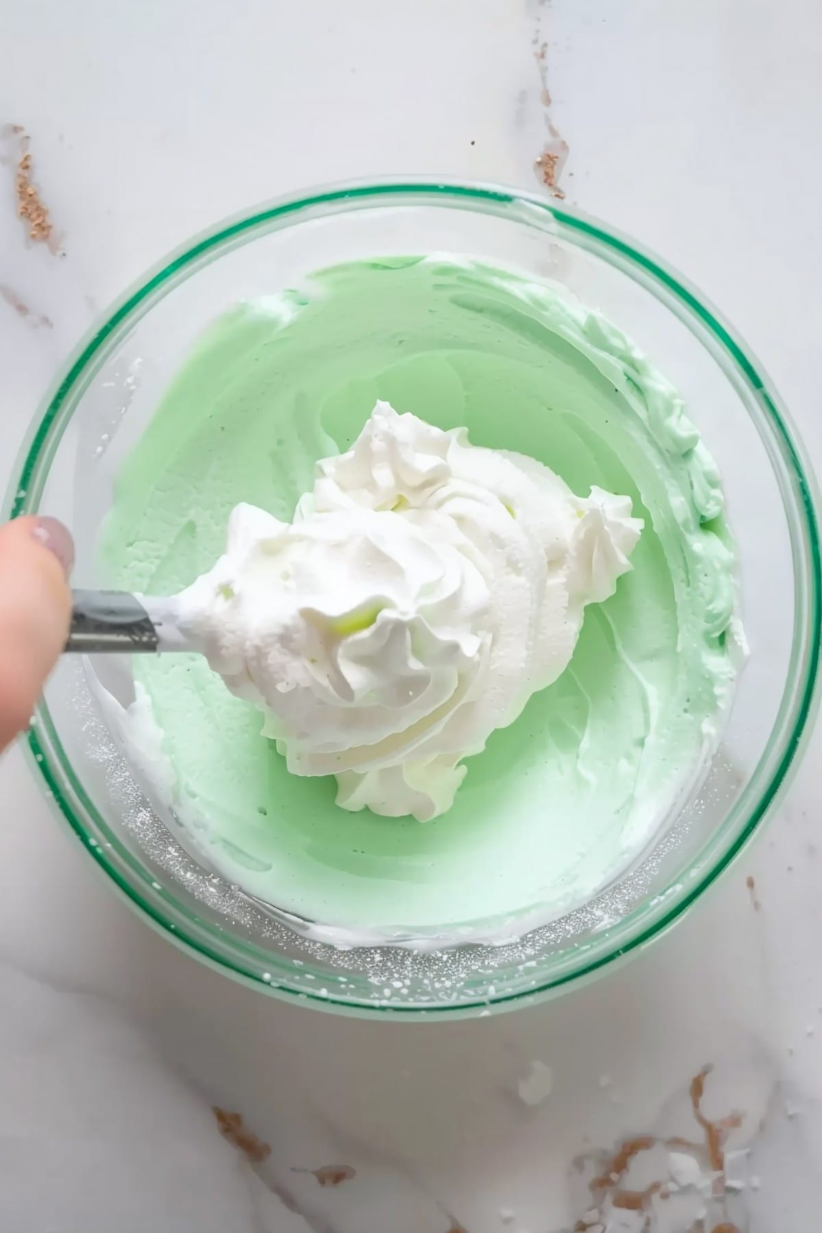 A large glass bowl of grasshopper pie filling with heavy cream on a marble countertop