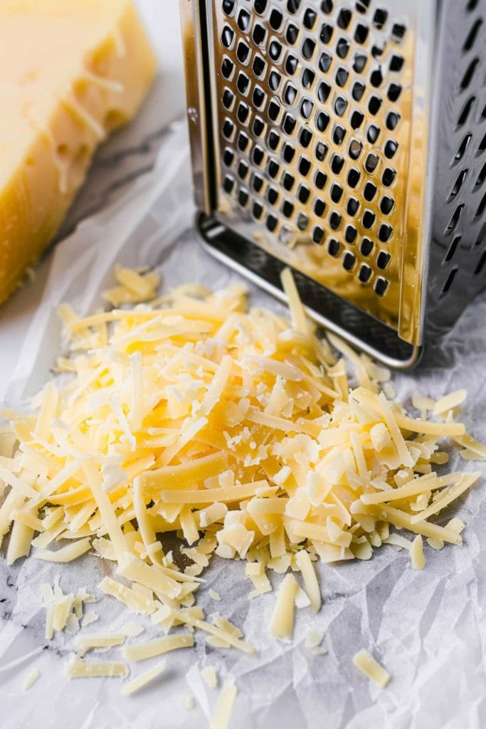 Cheese grater on white parchment paper  next to a grated cheddar