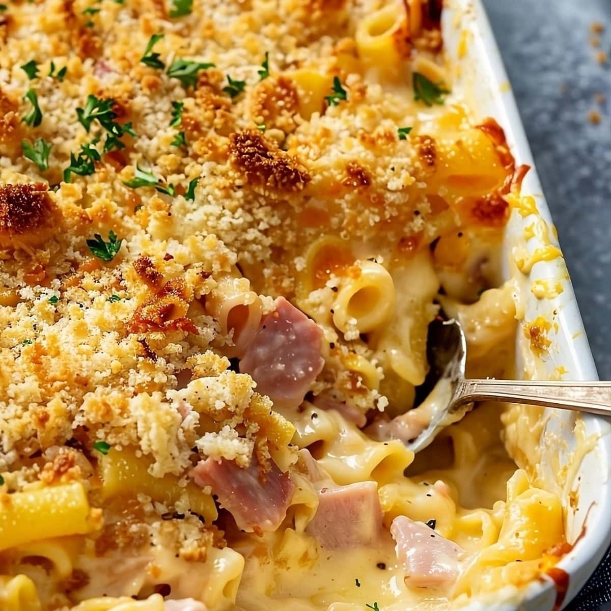 Cheesy ham and noodle bake with spoon in a baking dish.