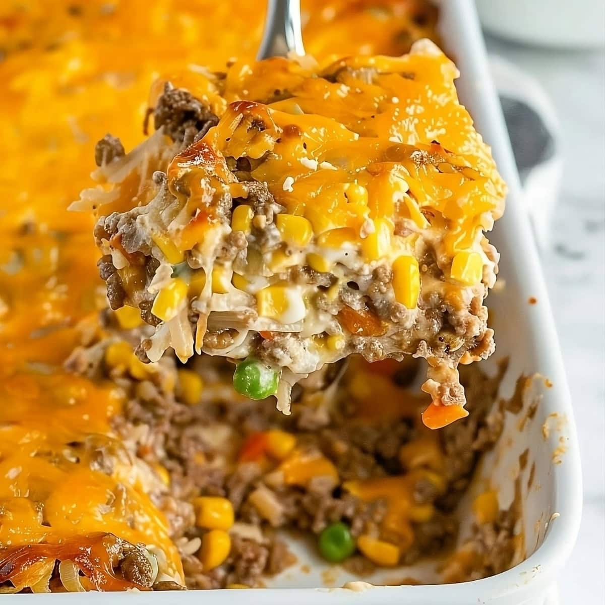 Hamburger hashbrown casserole with corn, carrots, green peas and melted cheese on top.