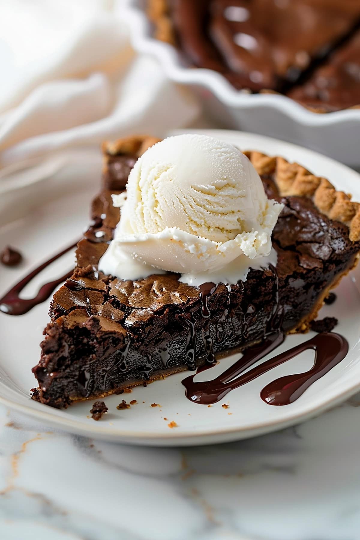 Flaky and buttery homemade brownie pie topped with a scoop of vanilla ice cream and drizzled with chocolate sauce