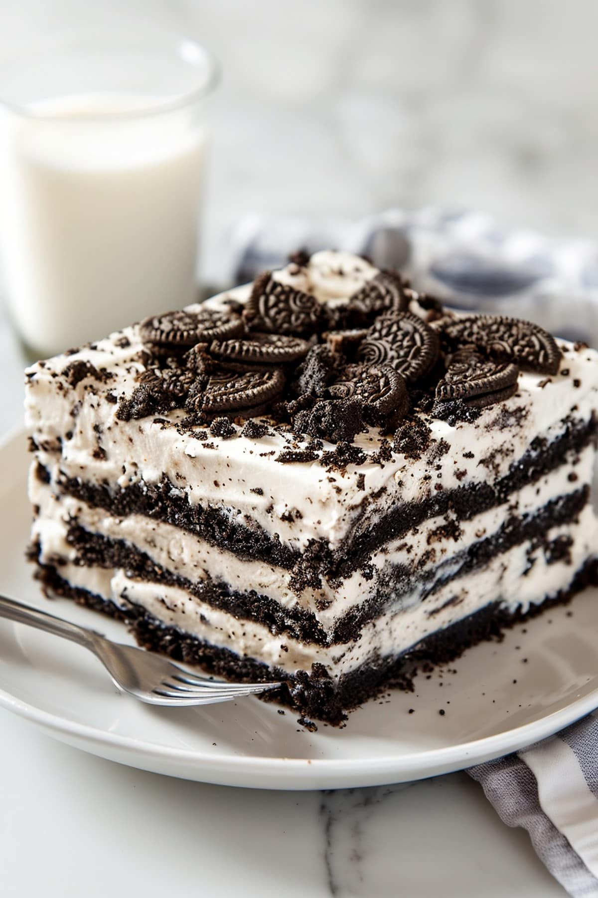 Slice of Oreo icebox cake showing layers of soft cookies and cream with extra crushed cookies on top