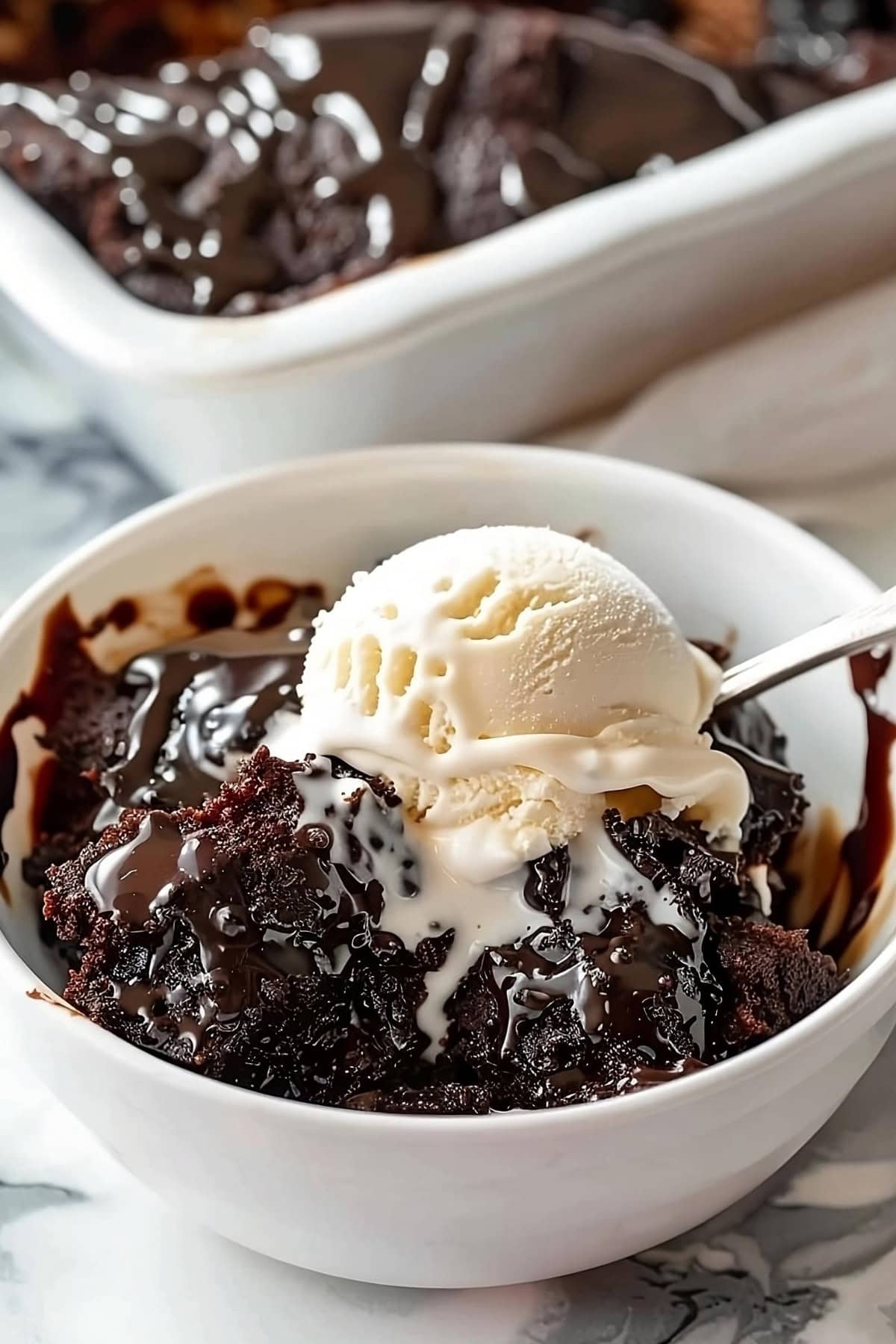 Chocolatey hot fudge cake topped with vanilla ice cream served in a white bowl.