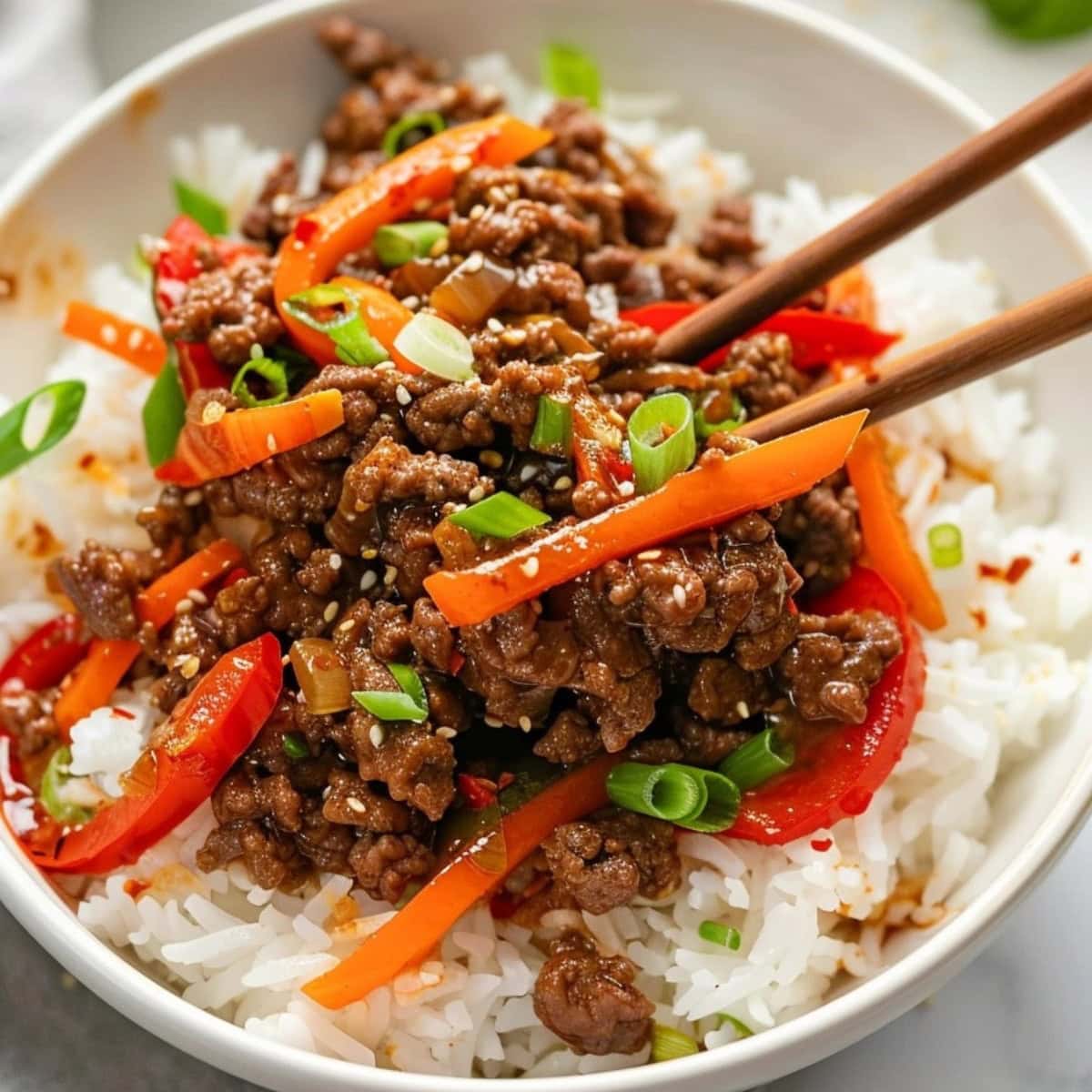 Chopsticks mixing beef with carrots, bell pepper and green onions topped on a white rice.