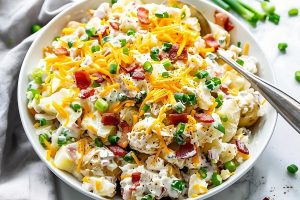 Bowl of loaded baked potato salad in a white bowl topped with grated cheese.