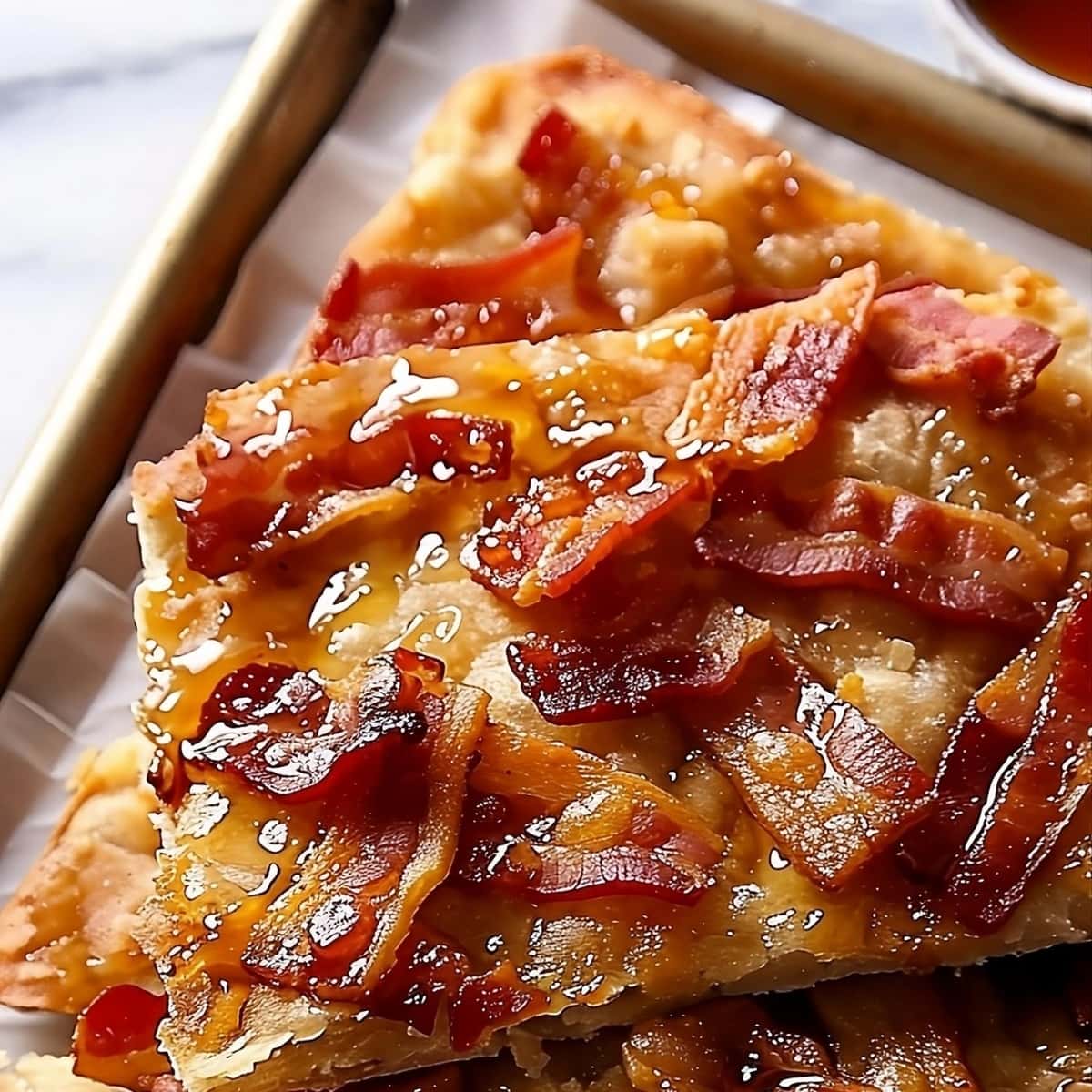 Sliced maple bacon crack in a baking sheet drizzled with maple syrup.