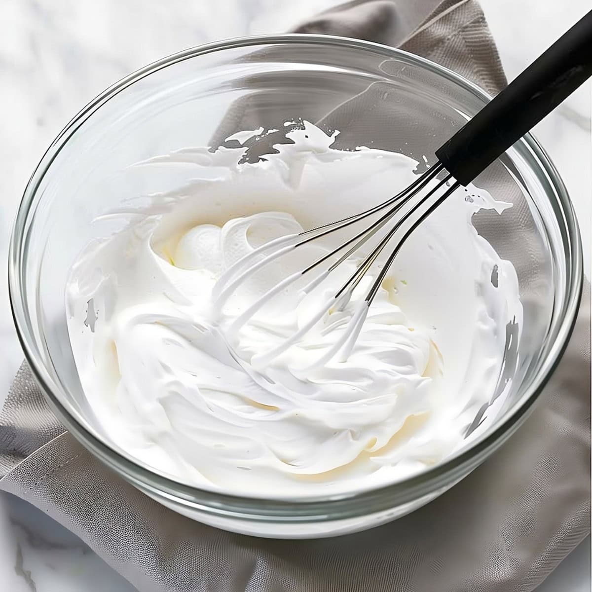 A glass bowl of marshmallow fluff with a whisk