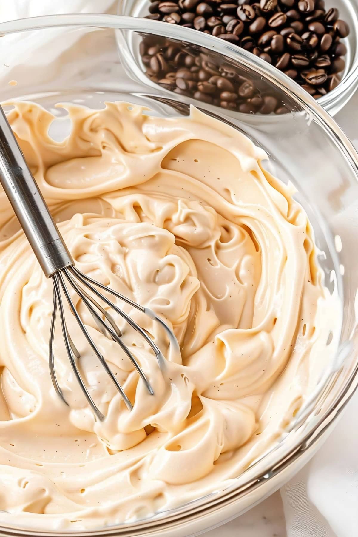 Coffee whipped cream being whisked in a bowl with a bowl of coffee beans on the side