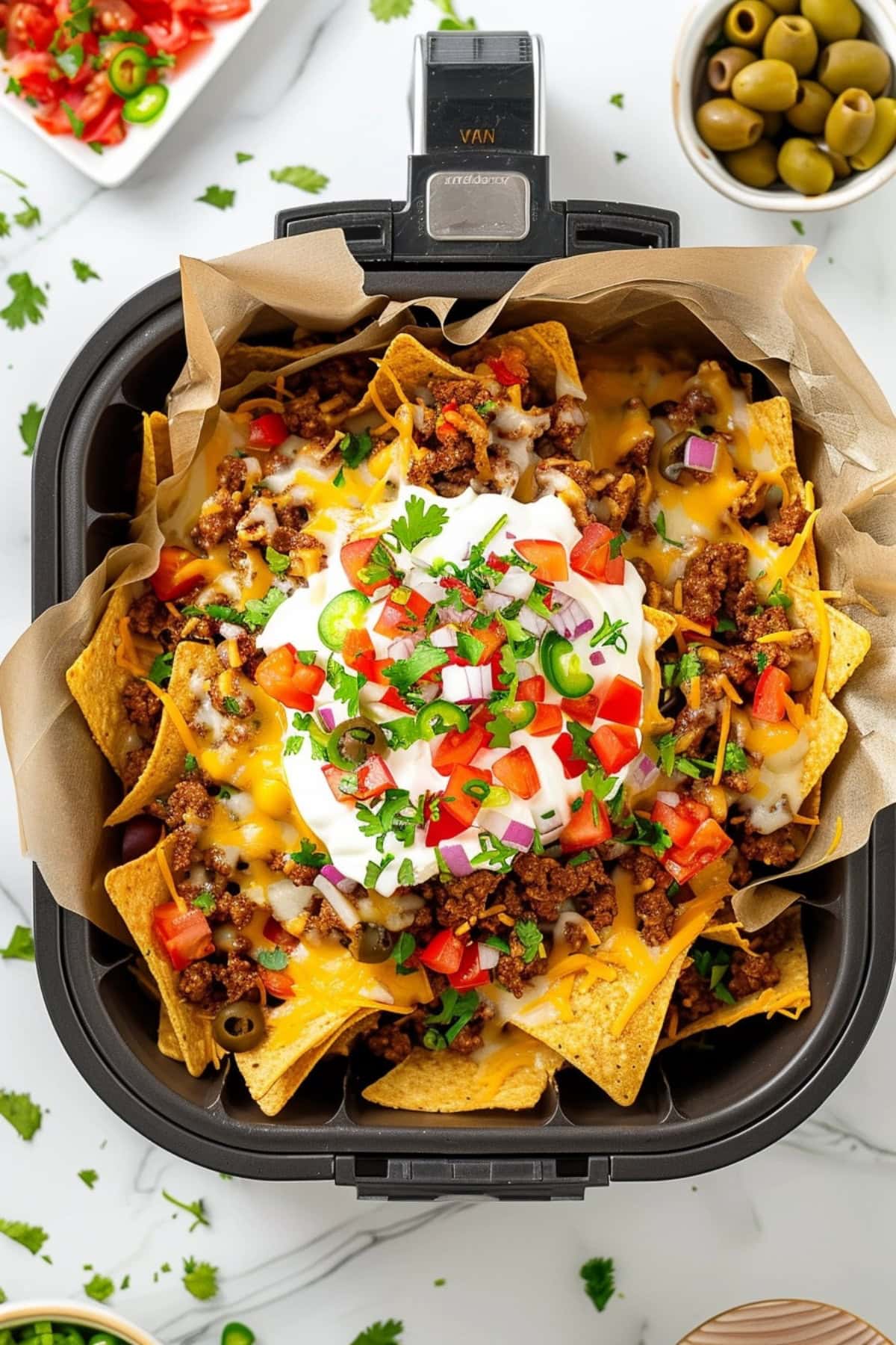 Loaded nachos in an air fryer with beef, tortilla chips, cheese, tomatoes, olive and sour cream.