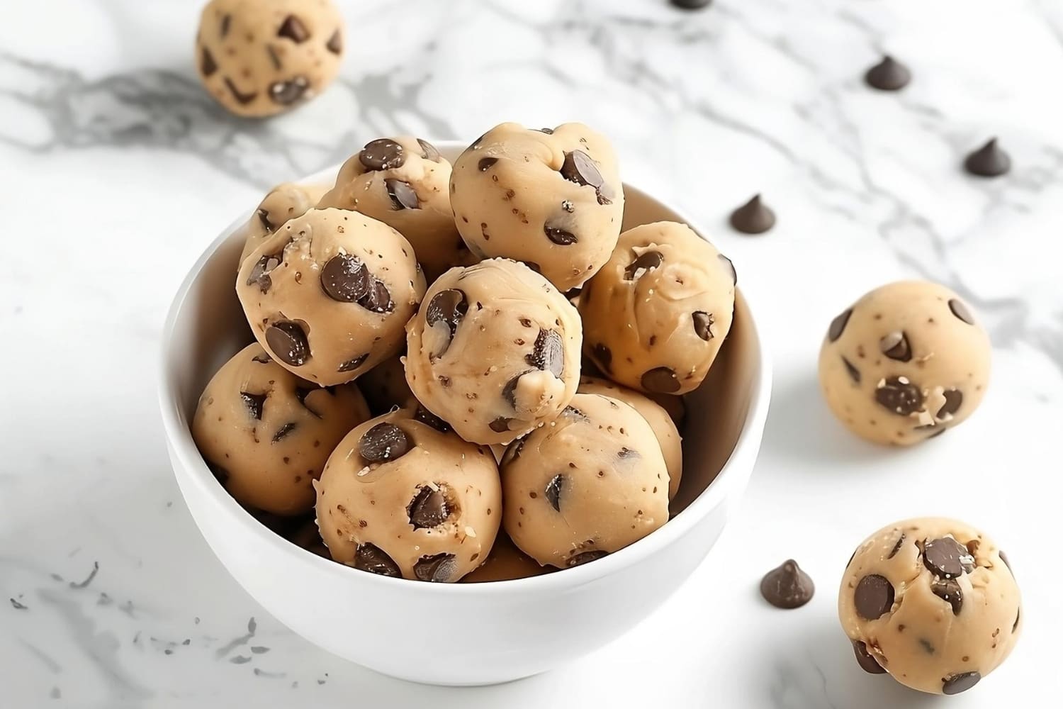 No bake cookie dough bites in a white bowl on a white marble surface.