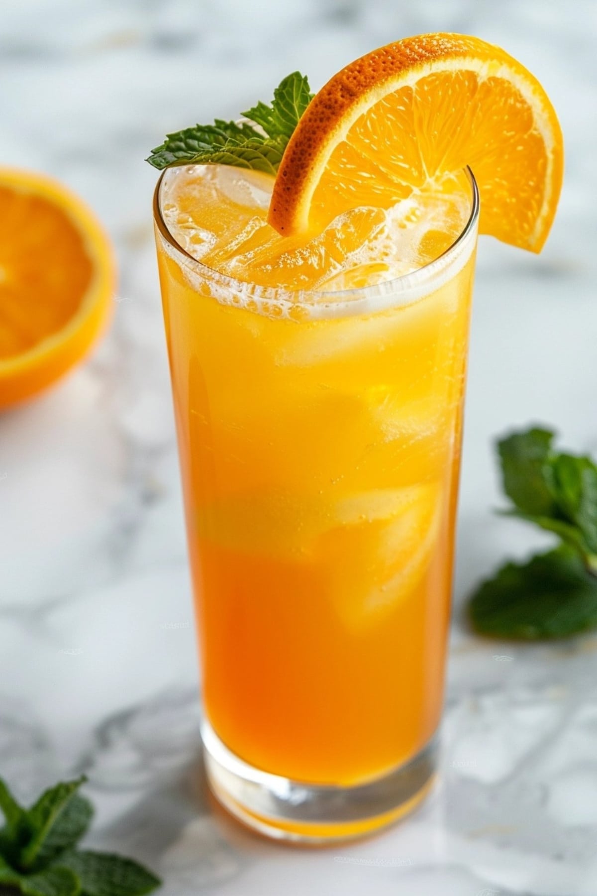 Filled with iced, orange crush cocktail in a high ball glass garnished with mint and orange slice.