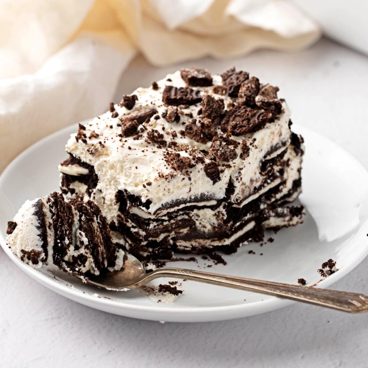 Oreo Icebox cake, a portion is taken out with a spoon in a white plate.