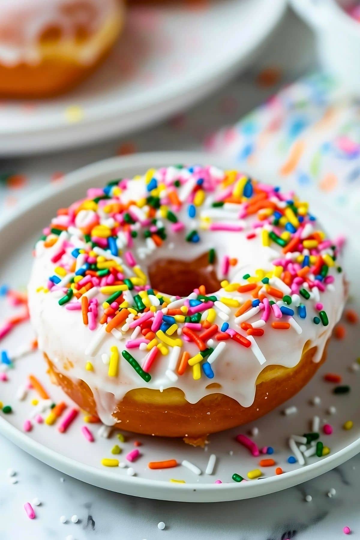 Donut with sugar glaze covered with colorful candy sprinkles served on a white plate.