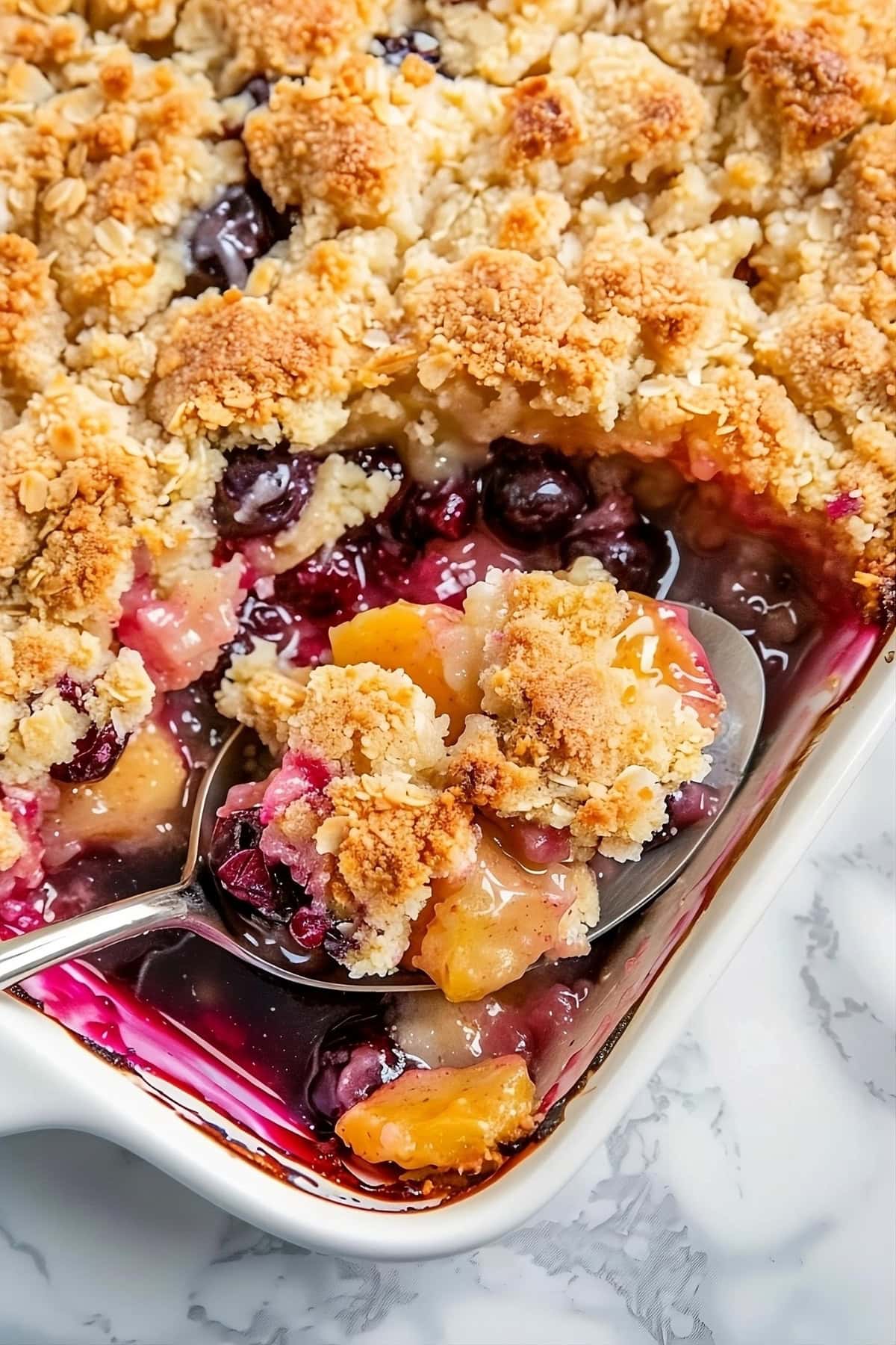 Peach and blueberry cobbler in a baking dish scooped by a spoon.
