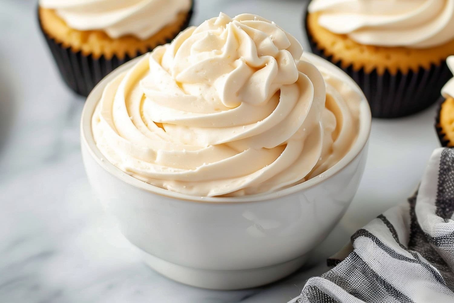 A bowl of homemade peanut butter frosting with vanilla cupcakes in the background