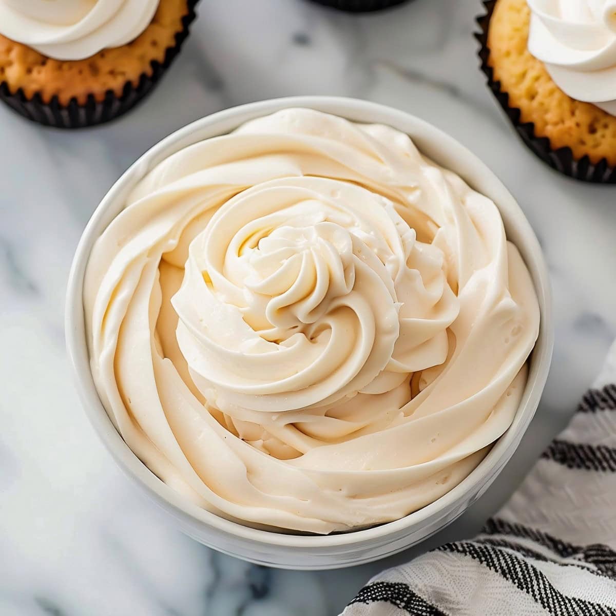 A white bowl filled with peanut butter whipped cream next to cupcakes