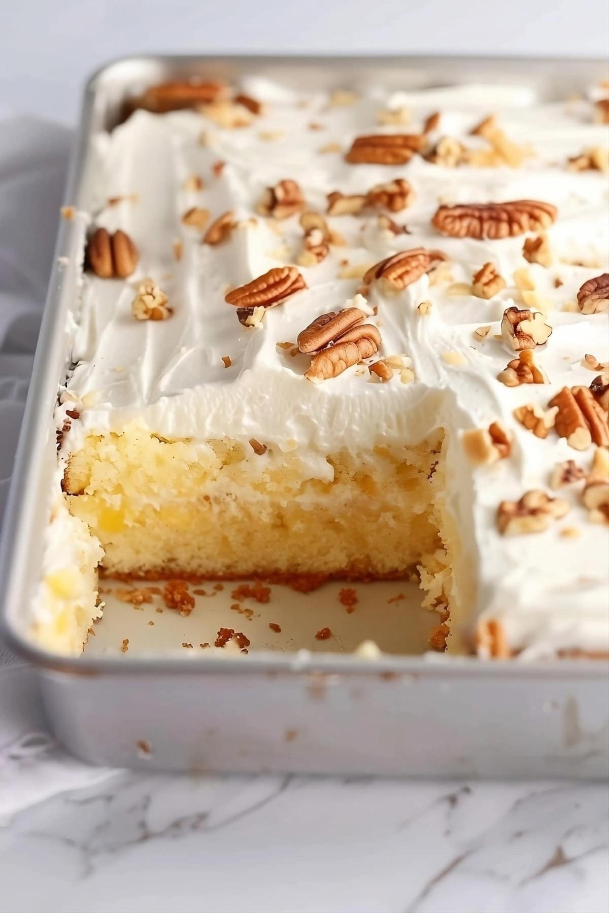 Pineapple cake baked in sheet pan topped with frosting and chopped pecans.