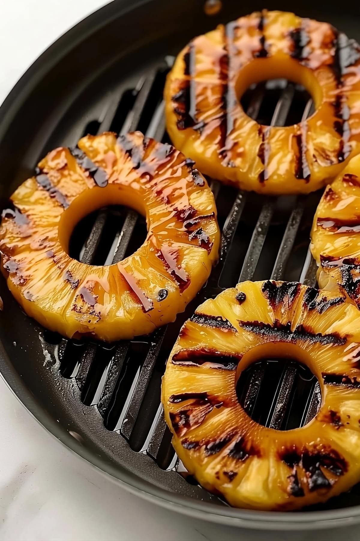 Pineapple rings grilled in a pan sitting on a white marble table.
