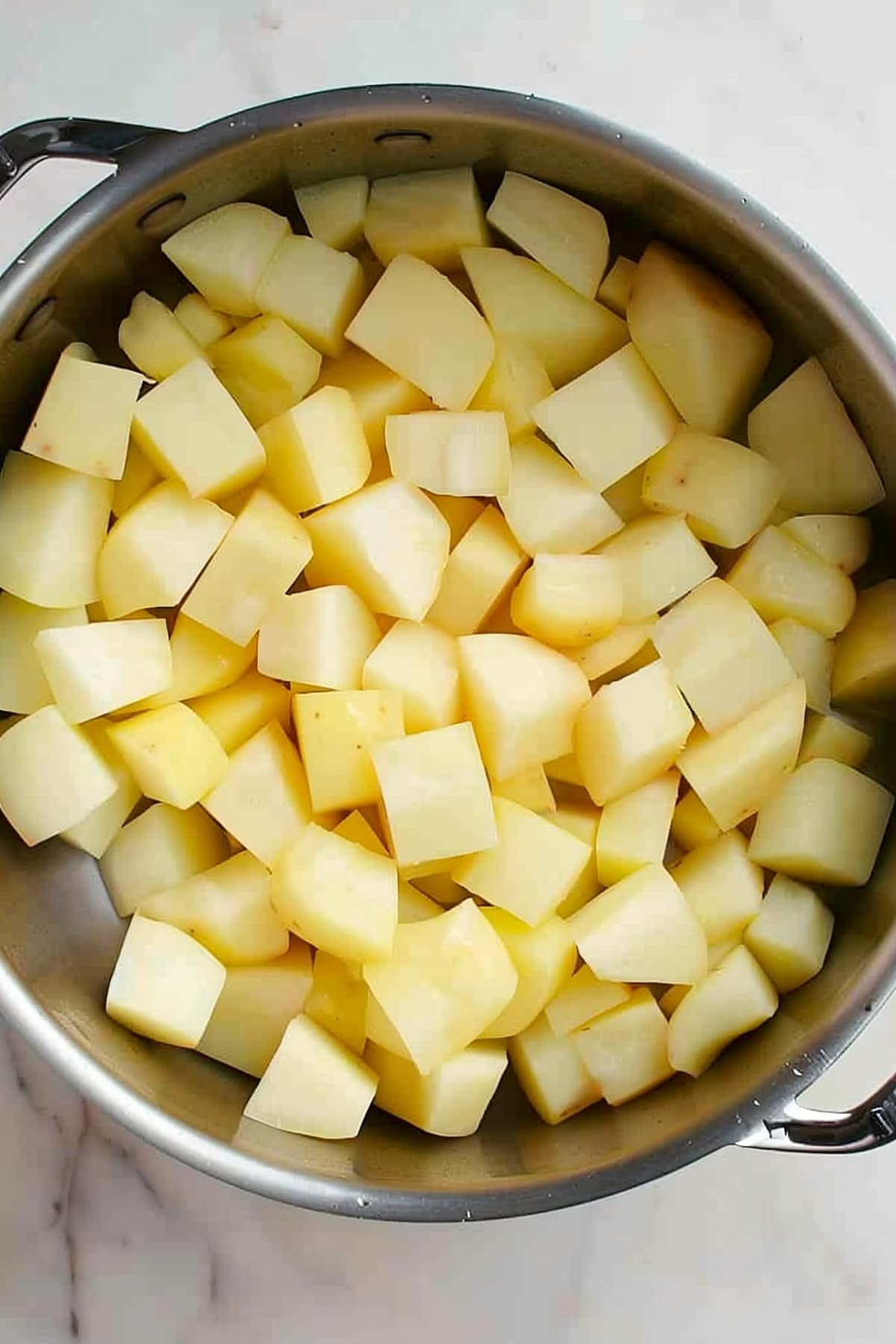 A pan filled with cubed potatoes on a marble counter