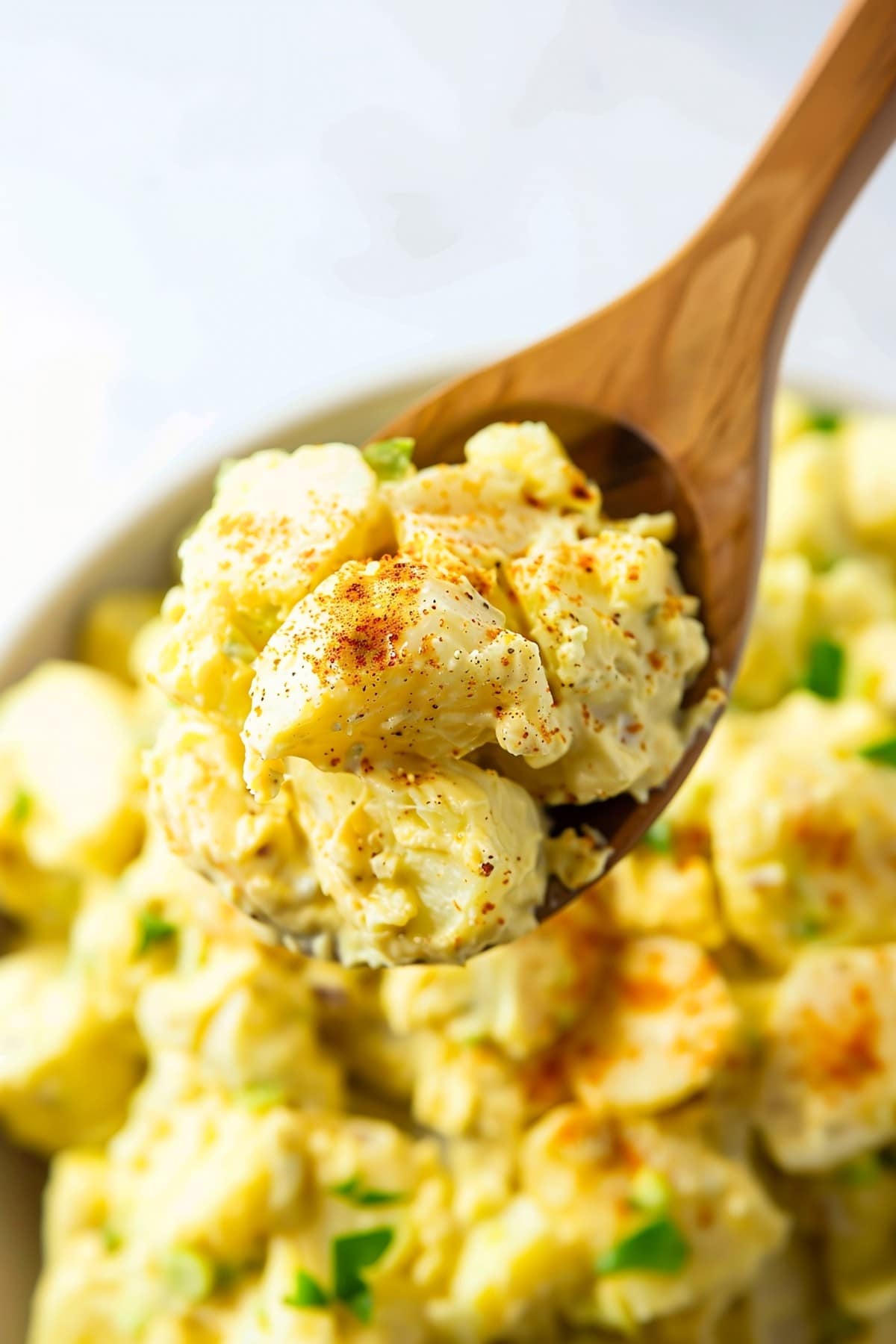 Hearty potato salad in a wooden spoon with a zesty deviled egg dressing, sure to please any crowd