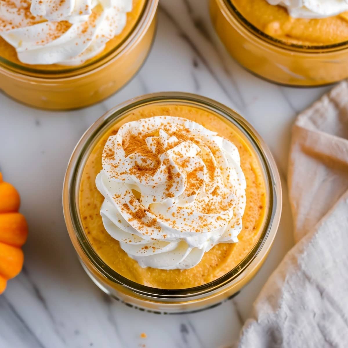 Three glasses of pumpkin mousse topped with whipped cream and cinnamon on top, top down view