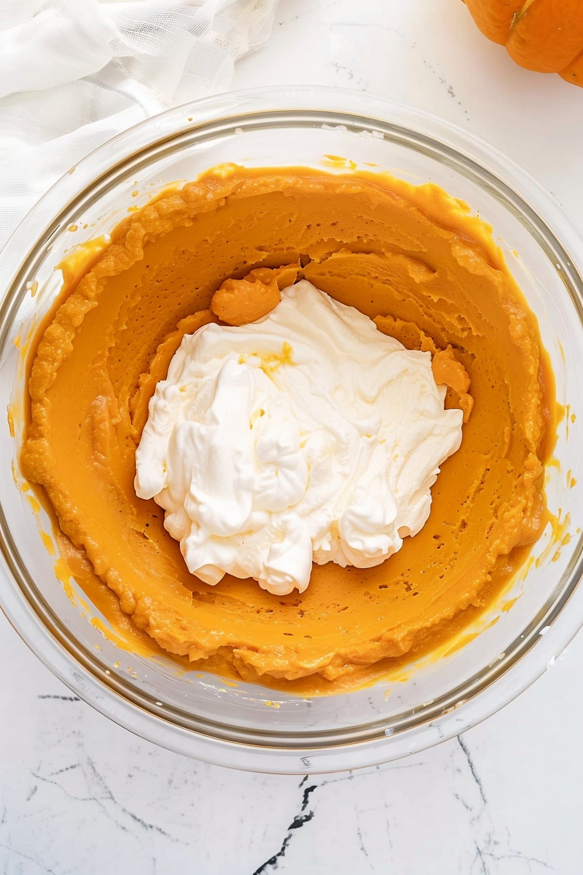 A large glass bowl of pumpkin pudding and whipped cream, overhead view