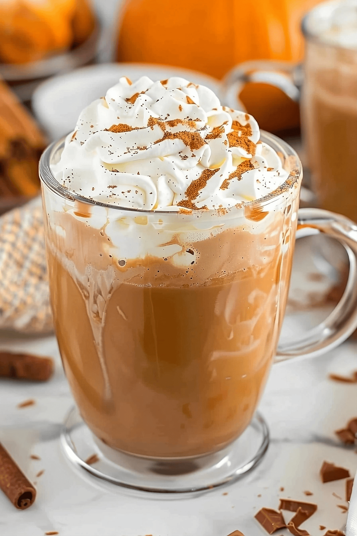 Pumpkin spice hot chocolate in a glass mug whit whipped cream and spices on top.