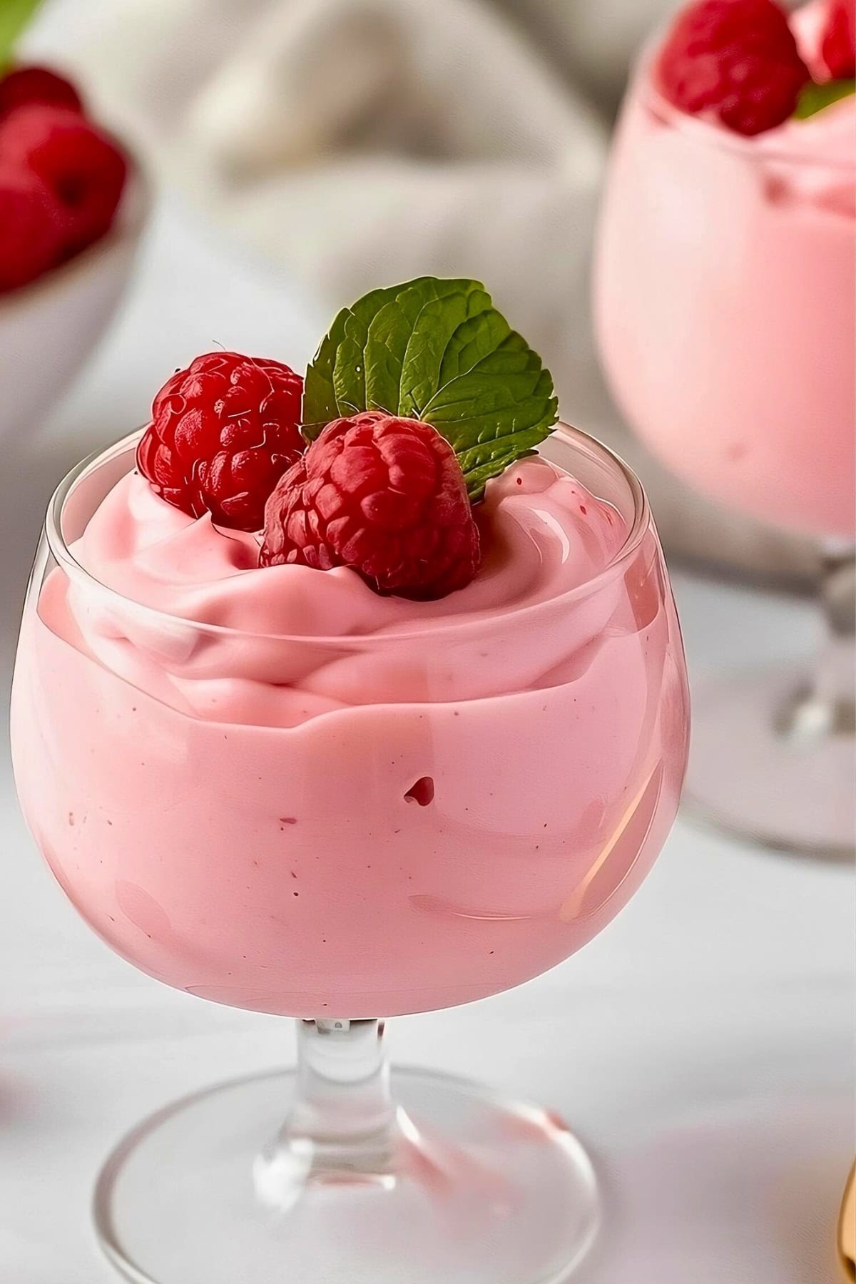 Dessert glass serving of raspberry mousse with fresh raspberries and mint leaf.
