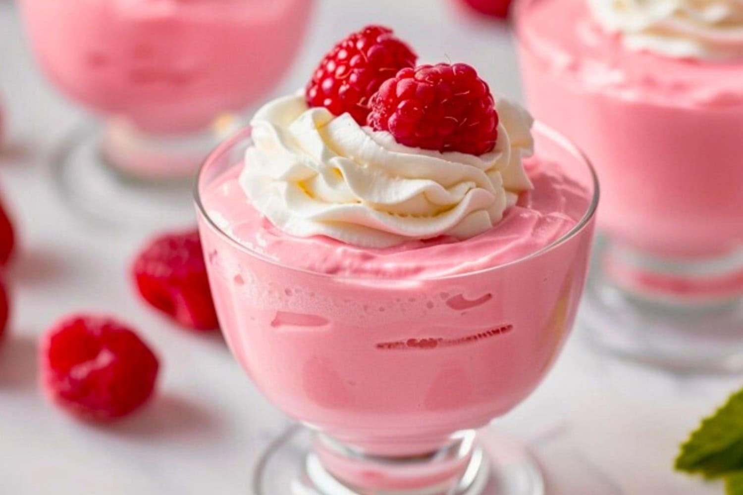 Raspberry mousse with whipped cream and raspberry garnish on top.