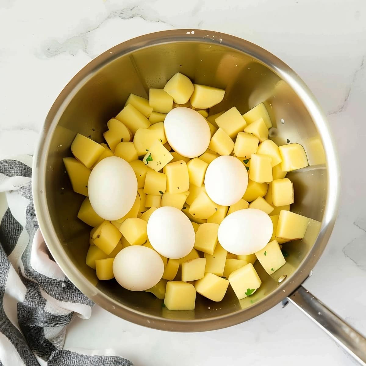 Cubed potatoes and eggs in a pan on a marble surface