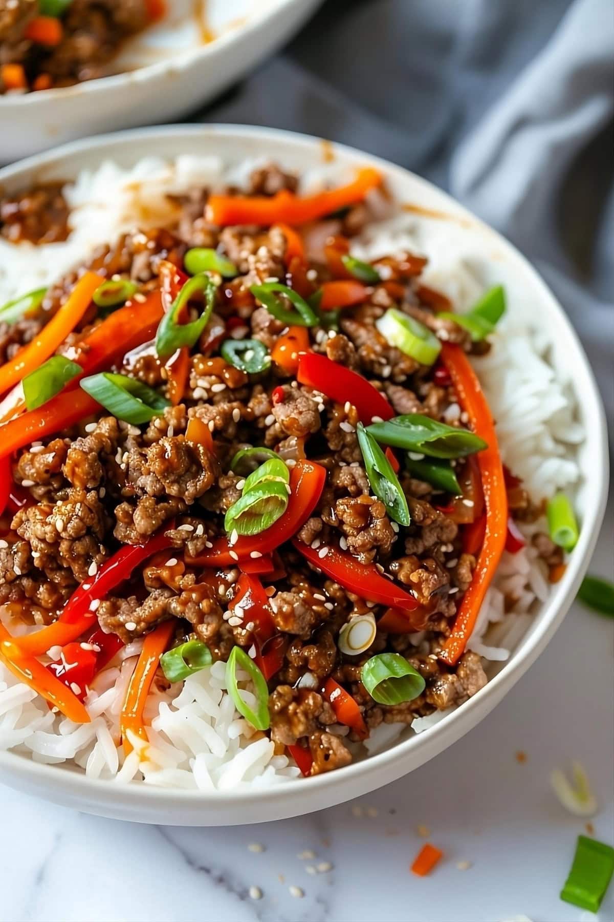 Korean beef bowl with ground beef, savory sauce, thinly sliced bell pepper and carrots served in a white bowl.