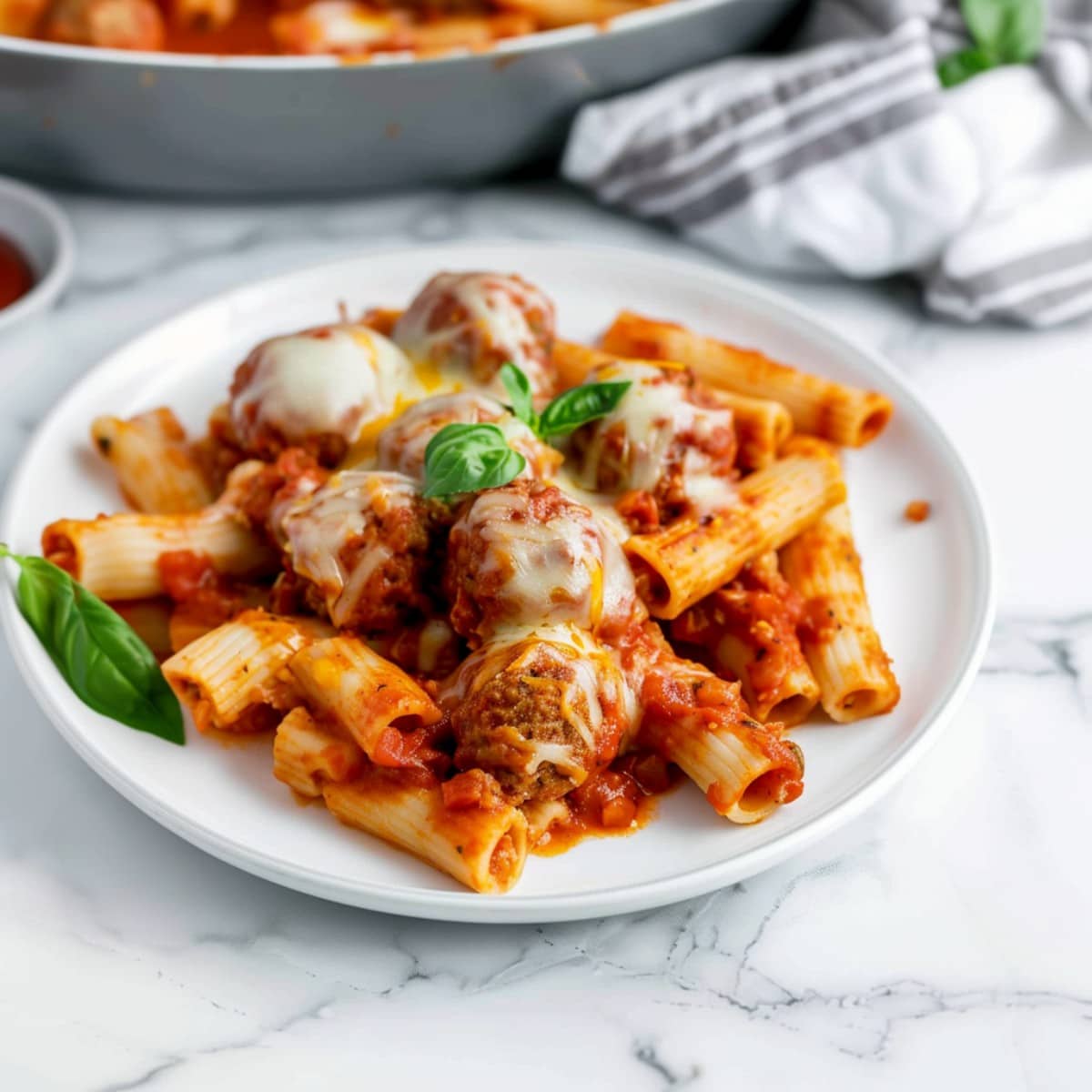 Comforting homemade meatballs and baked ziti pasta with tomato sauce and a hint of mint in a white plate