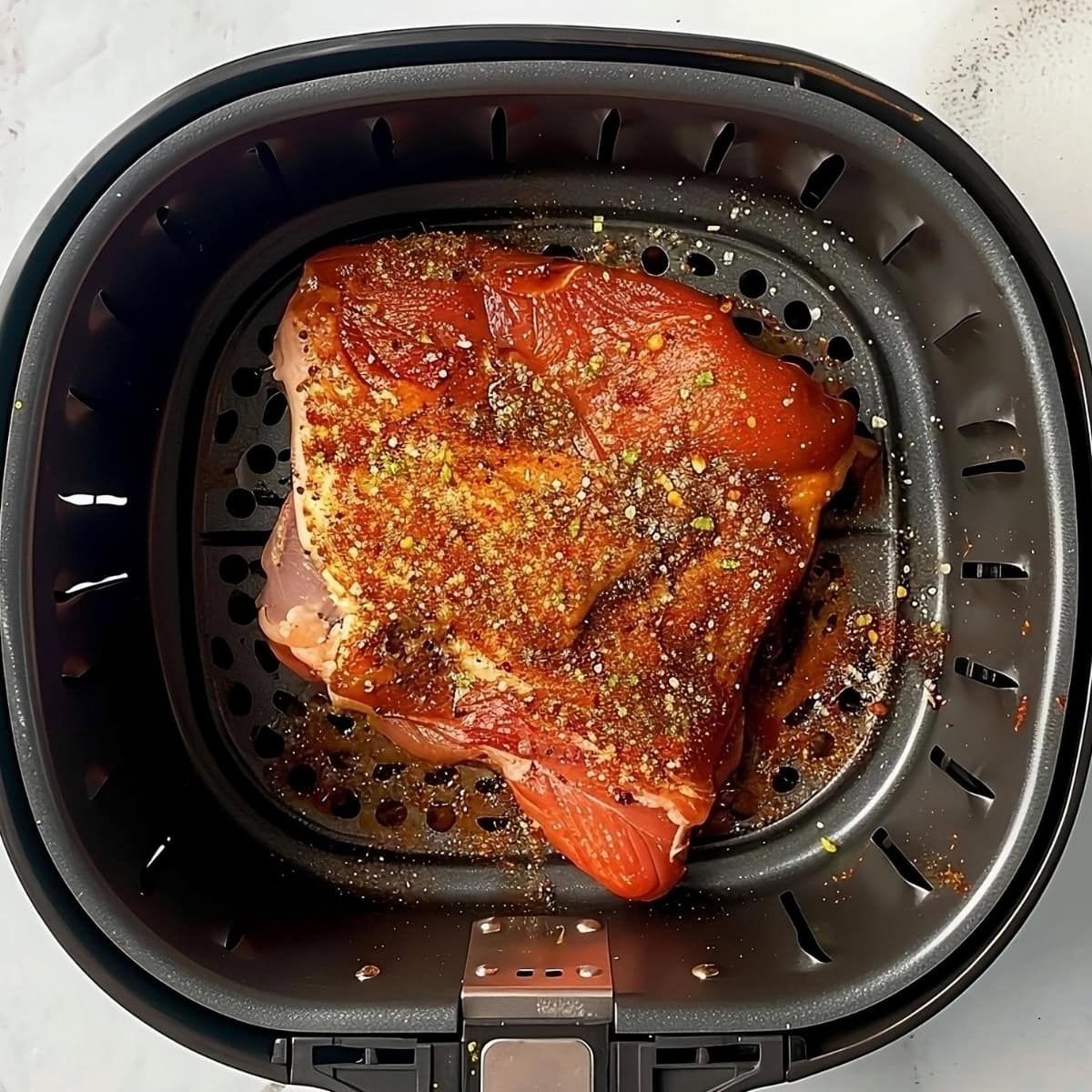 Pork meat seasoned with dry rubs spices placed inside an air fryer basket.