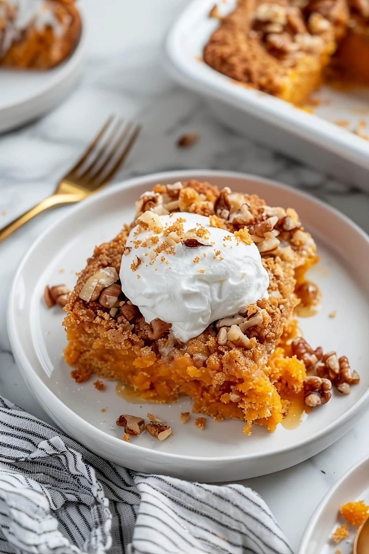A serving of sweet potato dump cake in a plate topped with whipped cream and chopped pecan nuts.