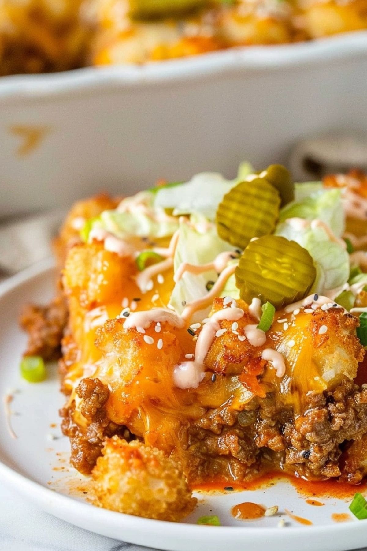 A slice serving of Big mac casserole with tater tots, onions, pickles, cheese, lettuce, and Thousand Island dressing.

