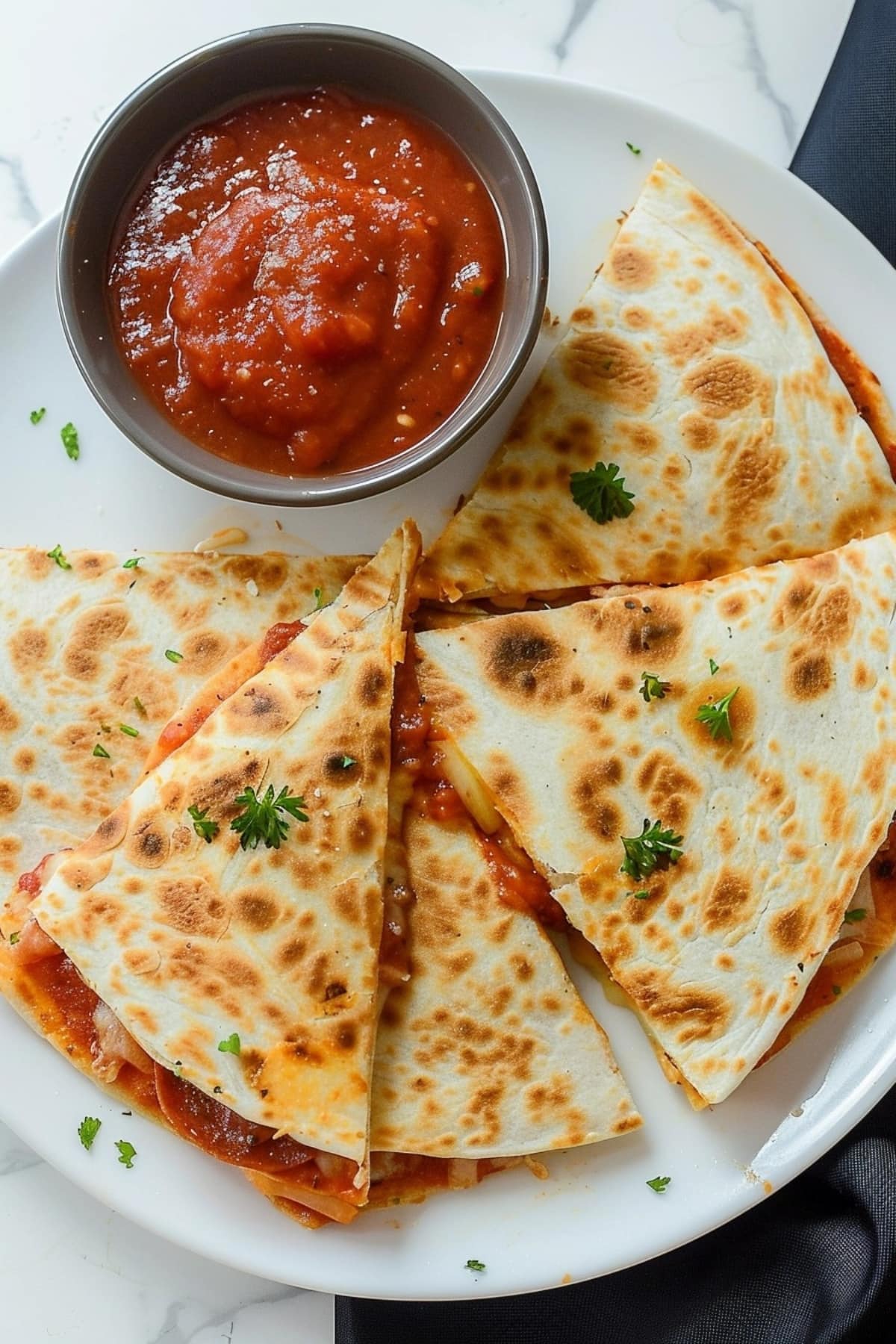 Cut in wedges pizza quesadillas with marinara sauce on a white plate.