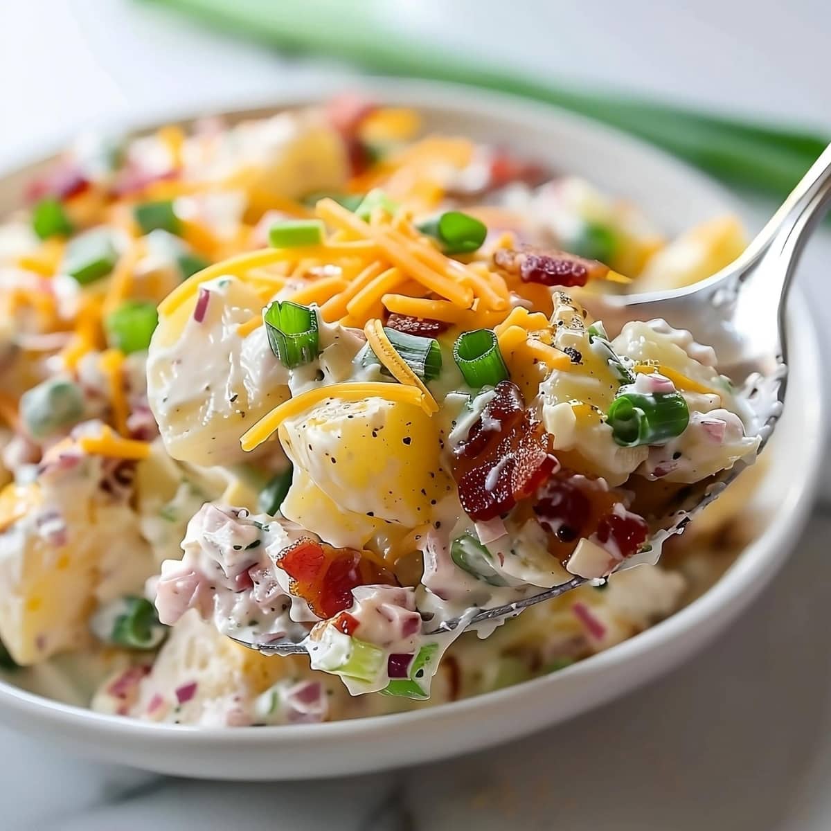 Spoonful of loaded baked potato salad with bacon, cheese and green onions.