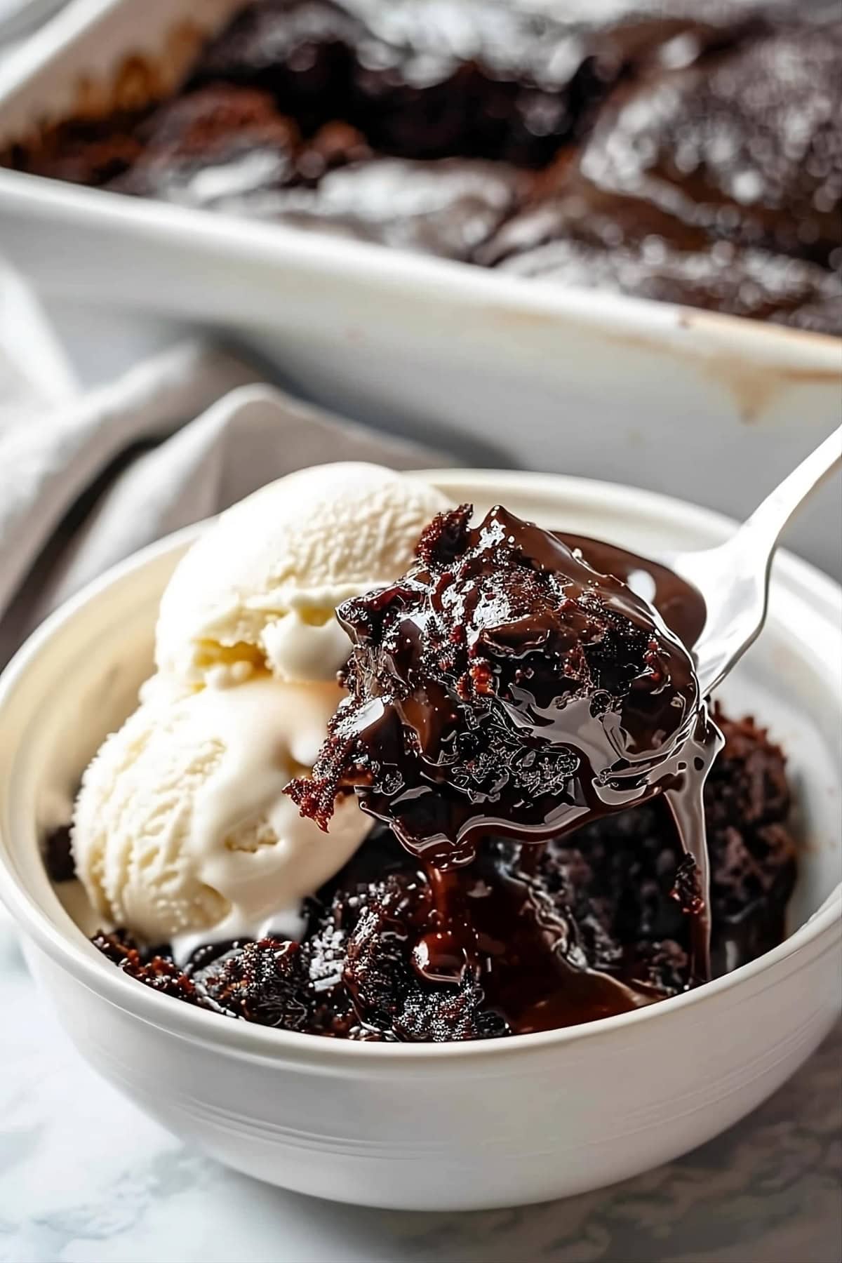 Spoon scooping a serving of gooey and chocolatey hot fudge cake from a white bowl.