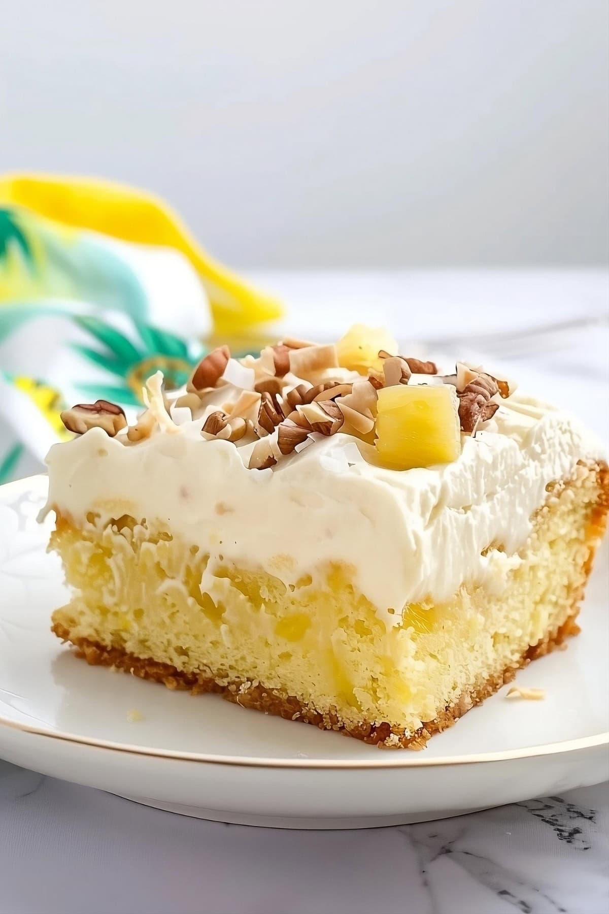 Slice of pineapple sheet cake topped with chopped pecans and pineapple chunks.