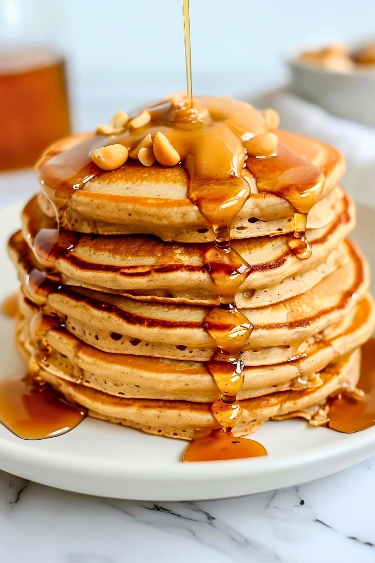 Stack of fluffy and thick peanut butter pancake drizzled with maple syrup and peanut butter spread on top.