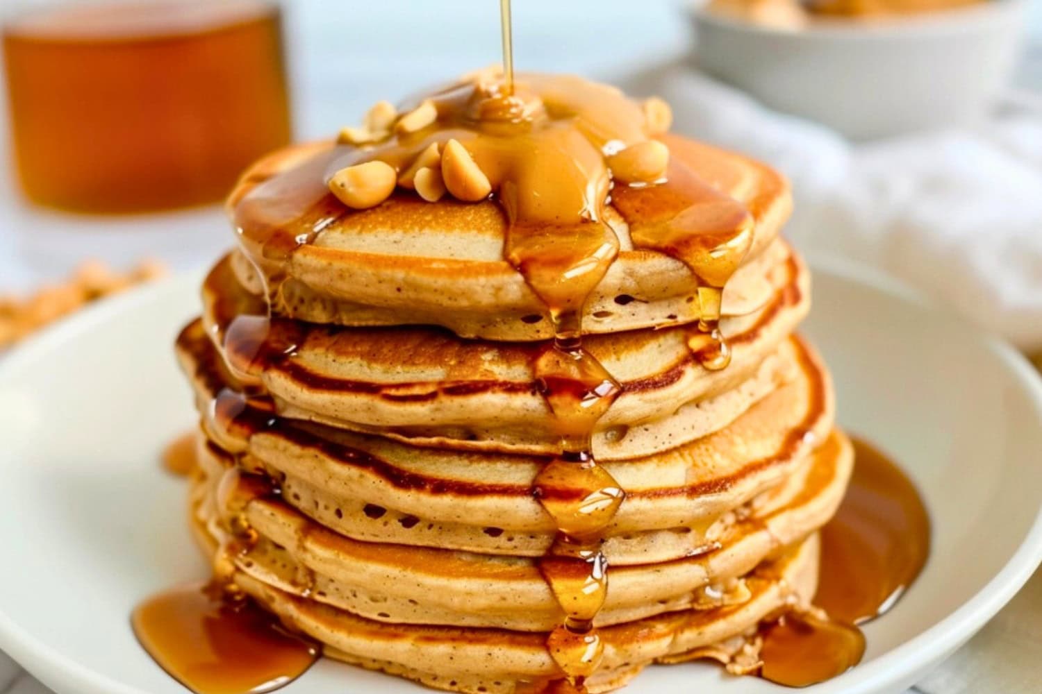 Stack of peanut butter pancake drizzled with maple syrup garnished with peanut butter and peanuts.